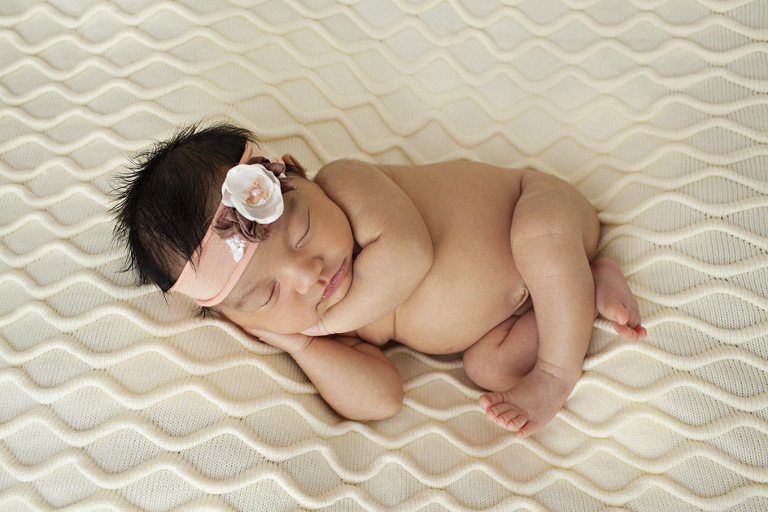 little newborn girl with pink headband on cream blanket